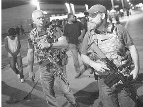 Oath Keepers, carrying rifles and wearing body armour, walk along West Florisant Avenue as demonstrators marking the first anniversary of the shooting of Michael Brown protest on Monday in Ferguson, Mo. Brown was shot and killed by a Ferguson police officer on Aug. 9, 2014.