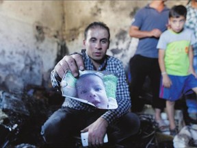 A relative holds up a photo of Ali Dawabsheh in a house that had been torched in a suspected attack by Jewish settlers in Duma village near the West Bank city of Nablus on Friday. The toddler died in the fire and his four-year-old brother and parents were injured according to a Palestinian official.