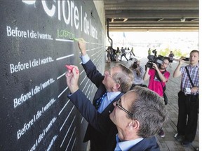 Saskatoon Mayor Don Atchison and Lorne Wright, foreground, write their goals on a chalkboard, Tuesday, as part of a new public art project under the Sid Buckwold Bridge after the announcement that both River Landing phases are now complete.