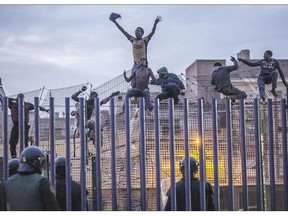 Spanish police officers watch would-be immigrants on a fence near Beni Enza, in the North African Spanish enclave of Melilla in March 2014. About 20,000 Africans tried to make the jump into Melilla last year.