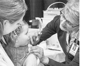 Tara Anderson holds her daughter Charlotte, who receives the flu vaccine from public health nurse Joan Kirkpatrick at Prairieland Park on Wednesday.