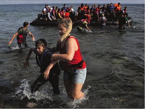 A volunteer helps a Syrian boy as he arrives with others at the coast on a dinghy after crossing from Turkey, at the island of Lesbos, Greece, Monday, The island has been transformed by the sudden new population of some 20,000 refugees and migrants, mostly from Syria, Iraq and Afghanistan.