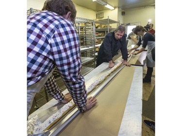 L-R: Keith Jorgenson, Randy Shaw and Anna Weinard help move the 19-foot long john to some tables, keeping it in the eavestrough where it was cooked, at Nestor's Bakery where students of the Community Learner's High School are attempting to make the world's longest long john donut, November 24, 2015. It measured in at just over 19' 1 1/2" long.