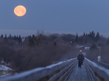 A rider on the Train Bridge pedestrian walkway at 33rd Street as the moon sets in the morning, February 4, 2015.