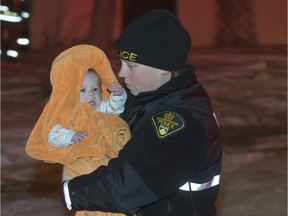 A Saskatoon police officer carries a baby to be checked out my MD Ambulance at the scene of a duplex fire in the 100 block of Imperial Street, Monday, November 30, 2015.