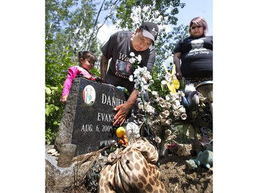 At the Sturgeon Lake grave site, Kevin Martell, with daughter Arielle, rubs his son Evanders grave stone, along with Nicole Daniels, Evanders mom and Irene Pete (grandmother) who visited their son's grave, June 12, 2015.