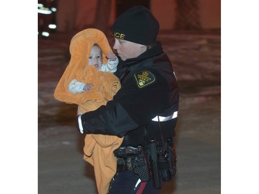 A Saskatoon police officer carries a baby to be checked out by MD Ambulance at the scene of a duplex fire on Imperial Street, November 30, 2015.