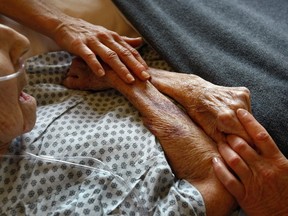 A hospice volunteer caresses the hands of terminally ill patient.