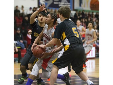 Justyn Lightle of the Bedford Road Collegiate RedHawks (red colours) drives the ball against Miguel Guevarra and Jordan Kashton of the Garden City Fighting Gophers during opening game action in the annual BRIT basketball classic, January 7, 2016.