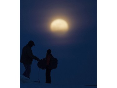 The full moon rising in the east appears just before these tobogganers' last run down Pest Hill, February 22, 2016.