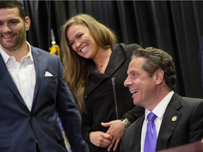 Gov. Andrew Cuomo, right, smiles with UFC athletes Chris Weidman, left, and Ronda Rousey after signing into law a bill that will allow professional mixed martial arts in New York, on April 14, 2016