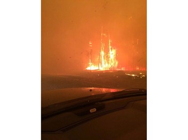 Fire burns near a road in Fort McMurray, Alberta on May 3, 2016. Raging forest fires whipped up by shifting winds sliced through the middle of the remote oilsands hub city of Fort McMurray Tuesday, sending tens of thousands fleeing in both directions and prompting the evacuation of the entire city.
