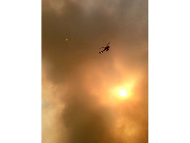 Smoke fills the air as a helicopter flies overhead in Fort McMurray, Alberta on May 3, 2016. Raging forest fires whipped up by shifting winds sliced through the middle of the remote oilsands hub city of Fort McMurray Tuesday, sending tens of thousands fleeing in both directions and prompting the evacuation of the entire city.