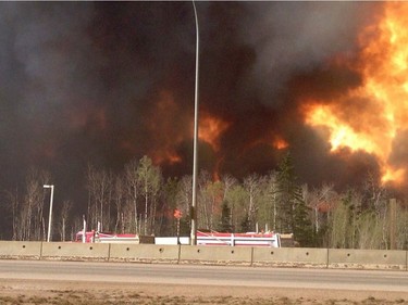 Trees burn near a road in Fort McMurray, Alberta, May 3, 2016 in this image provide by radio station CAOS91.1. At least half of the city of Fort McMurray in northern Alberta was under an evacuation notice Tuesday as a wildfire whipped by winds engulfed homes and sent ash raining down on residents.