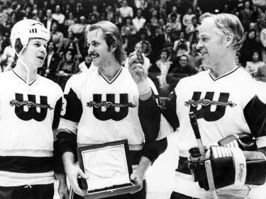 Gordie Howe of the Hartford Whalers of the World Hockey Association looks at a puck presented to him by his sons Mark (L) and Marty (C) before a game in December 1977.