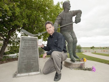 Ron Sekulich kneels for a photograph, while holding a Godie Howe rookie card, with the Gordie Howe statue outside of Sasktel Centre in Saskatoon, June 10, 2016. Howe passed away today at the age of 88.