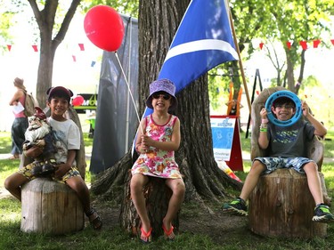 Aiden, Mira and Nyle Voralia sit on handmade stump chairs at the PotashCorp Children's Festival at Kiwanis Park Sunday in Saskatoon.