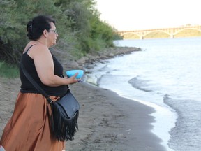 Jackie Crowe makes an offering to the South Saskatchewan River during a water song ceremony on Wednesday night. One of the organizers of the event, she said the ceremony will take place everyday until the Husky Energy Inc. oil spill in the North Saskatchewan River is cleaned up and its investigation concluded. She's also part of a group of Saskatoon residents who are organizing a water drive for homeless people in the affected communities. (Morgan Modjeski/The Saskatoon StarPhoenix)