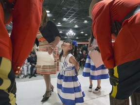 A smiling little girl looks up at a couple smiling RCMP officers after becoming a Canadian at a Citizenship ceremony with Officer of the Order of Canada Arnold Boldt in Saskatoon at the Western Development Museum on Canada Day on July 1, 2016.