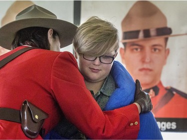 Ten-year-old Luca Bourdages, who spoke and read a poem in memory of his father Marc Bourdages, whose photo is in the background, receives hugs from all the RCMP officers attending the 10-year memorial for two RCMP officers who were tragically killed in 2006, July 6, 2016.