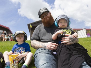 Katlin Barker (center) and his two sons Logan (right) and Royce (left) sit on the grass while waiting for the Monsters and Mayhem show to begin at the Wyant Group Raceway in Saskatoon, Saskatchewan on Saturday, July 16th, 2016.