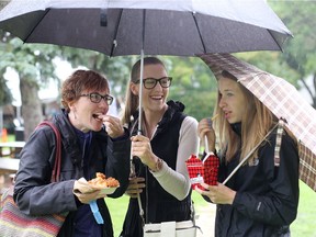 Vanessa, from left, Cortney and Amy Nyssen try out food from Smoke's Poutinerie under their umbrellas at Taste of Saskatchewan in Saskatoon on Tuesday.
