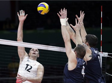 Canada's Gavin Schmitt (12) spikes the ball as United States' David Lee, center, and Matthew Anderson, right, attempt to block during a men's preliminary volleyball match at the 2016 Summer Olympics in Rio de Janeiro, Brazil, Sunday, Aug. 7, 2016.