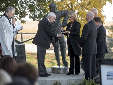 Saskatoon Funeral Home director Bill Edwards, left, helps, Cathy Howe, daughter of Mr. Hockey Gordie Howe, places his ashes before they are interned to the base of a statue of him, as her brothers Marty, Mark, and Murray look on during a memorial service outside Sasktel Centre in Saskatoon, Sunday, September 25, 2016.