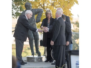 Saskatoon Funeral Home director Bill Edwards, left, helps, Cathy Howe, daughter of Mr. Hockey Gordie Howe, places his ashes before they are interned to the base of a statue of him, as her brothers Marty, Mark, and Murray look on during a memorial service outside Sasktel Centre in Saskatoon, Sunday, September 25, 2016.