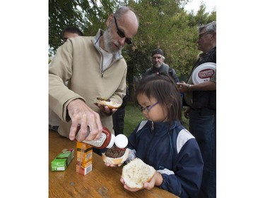 People lined up in Victoria Park for burgers and drink, along with live music and balloons, September 5, 2016, during the Saskatoon & District Labour Council's Labour Day BBQ in the park. Rodney Mercer helps six-year-old granddaughter Dakota Mercer get her burger ready.