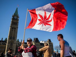 A woman waves a flag with a marijuana leef on it next to a group gathered to celebrate National Marijuana Day on Parliament Hill in Ottawa, Canada on April 20, 2016.