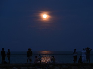 Locals watch the supermoon rise over the ocean at a beach in Sanur on Indonesia's resort island of Bali on November 14, 2016. Skygazers headed to high-rise buildings, ancient forts and beaches on November 14 to witness the closest "supermoon" to Earth in almost seven decades, hoping for dramatic photos and spectacular surf. The moon will be the closest to Earth since 1948 at a distance of 356,509 kilometres, creating what NASA described as "an extra-supermoon."