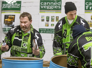 Saskatchewan Rush President Lee Genier with Rush players Nik Bilic and Brett Mydske, wearing their ugly Christmas sweater jerseys, were spending time at the Saskatoon Food Bank helping out Executive Director Laurie O'Connor to sort barrels of food delivered during this peak Christmas rush season, December 15, 2016.