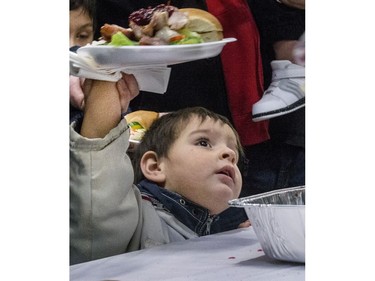 J.R. Thomas looks up to a volunteer standing in line holding up his plate with his mom at the Saskatoon Tribal Council's annual Community Christmas Celebration at the White Buffalo Youth Lodge where hundreds of community members join the celebration with a hot turkey dinner and a special visit from Santa Claus for families in need, December 15, 2016.