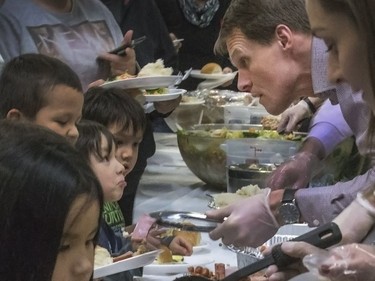 A little guy with a long bottom lip looks to mayor Charlie Clark in line at the Saskatoon Tribal Council's annual Community Christmas Celebration at the White Buffalo Youth Lodge where hundreds of community members join the celebration with a hot turkey dinner and a special visit from Santa Claus for families in need, December 15, 2016.
