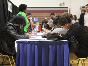 People attending the WEconnect job fair, hosted by the Saskatoon Open Door Society, fill out forms at the event's applications table on Wednesday. Taking place at Marion M. Graham Collegiate, organizers estimate 1,600 people stopped by the event, which aimed to connect global talent with local employers.