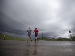 Karsten Hoehn, left, and Chris Prychak run along a path near the Sid Buckwold Bridge as heavy rain clouds move into Saskatoon, Sask. on Thursday, May 25, 2017.