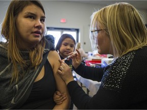 Sophia Brandon (C) watches her mother Tricia Clearsky receive a Flu Shot during an Immunization clinic at Station 20 West in Saskatoon on Oct. 23, 2017.