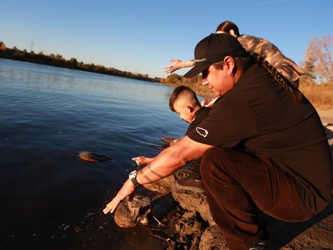 Randy Morin sprinkles tobacco into the river with his nine-year-old son Keesik, four-year-old daughter Kisay and partner Lindsay Knight as an offering in Saskatoon.