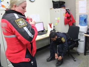 Community Support Officer (CSO) Jill Meldrum, left, attaches a name tag to her bright-red CSO uniform while Jonathan Keens-Douglas, right, adjusts his uniform as they prepare for a 10-hour shift in Saskatoon on Nov. 30, 2017.