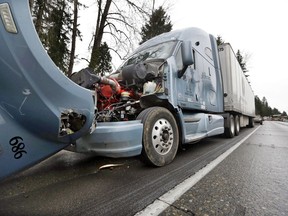 A semi-truck with visible damage to its hood sits parked on the shoulder just ahead of a car covered in mud and debris and with a smashed windshield just beyond where an Amtrak train lay spilled onto Interstate 5 below as some train cars remain on the tracks above Monday, Dec. 18, 2017, in DuPont, Wash. The Amtrak train making the first-ever run along a faster new route hurtled off the overpass Monday near Tacoma and spilled some of its cars onto the highway below, killing some people, authorities said.