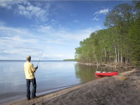 "Canoe resting on the lake shore. man fishing, Prince Albert National Park. Saskatchewan." Model and Property Released