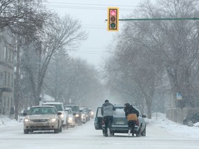 A group of people push a car through the Clarence Avenue and 8th Street intersection during a snowstorm in Saskatoon, SK on February 14, 2018.