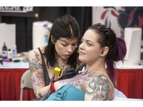 Sam Smith (left), who works at Scythe & Spade tattoo shop in Calgary, works on Evelyn Arnason, also a tattoo artist at Ink Addiction in Saskatoon, for a large tattoo on her chest during the Saskatoon Tattoo Expo at Prairieland Park in Saskatoon, SK. on Saturday, April 11, 2015.