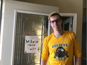 Xavier LaBelle returns home after spending several weeks in the hospital recovering from the April 6 bus crash that resulted in the deaths of 16 people. Behind him, a hand-written sign that reads "Welcome Humboldt Broncos Home Xavier." In the photo, LaBelle sports a Humboldt Broncos shirt and a large smile.