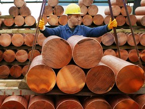 Workers use a hoist to stack copper ingots.