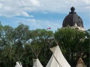 A Canadian flag flaps in the wind as the dome of the Saskatchewan Legislative Building looms above the trees. Beneath, teepees occupy the park as part of the the Justice for our Stolen Children camp.