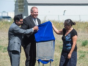 Janine Windolph, right, Gene Makowsky, Minister of Parks, Culture and Sport, at centre, and land owner Nadeem Islam unveil a plaque marking the Regina Indian Industrial School Cemetery on Pinkie Road as provincial heritage property.