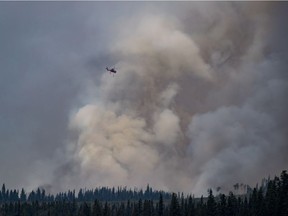 A helicopter being used to fight a smaller fire nearby flies past a large plume of smoke rising from a wildfire near Fraser Lake, B.C., on Wednesday August 15, 2018. The British Columbia government has declared a provincial state of emergency to support the response to the more than 500 wildfires burning across the province.