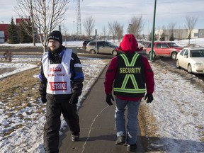 A striking Saskatoon Co-op employee, left, passes a private security guard on a picket line near Attridge Drive.